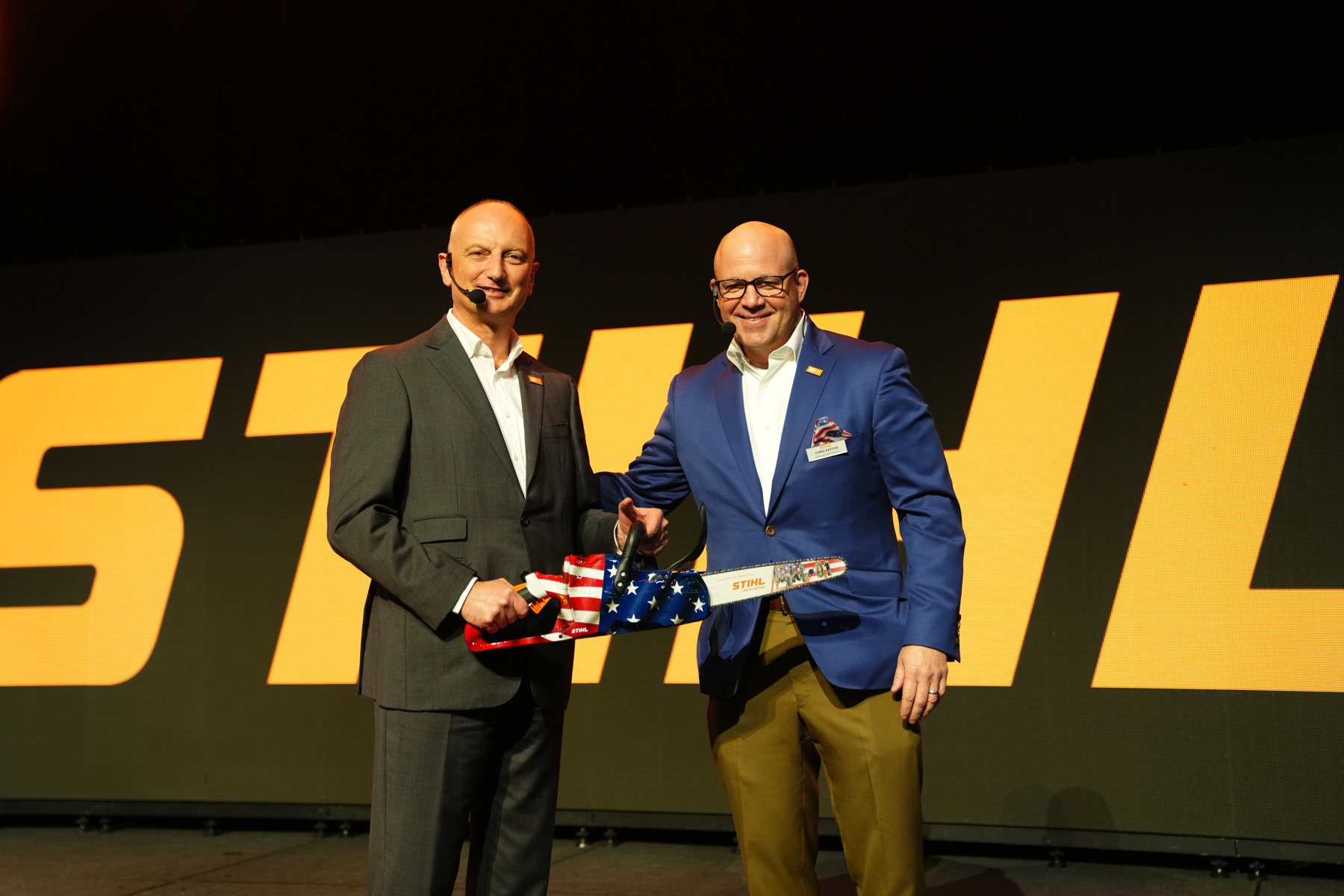 Il dott. Nikolas Stihl (a sinistra) e Chris Keffer, amministratore delegato di STIHL Inc. negli Stati Uniti, presentano una sega per l'anniversario con una bandiera statunitense.